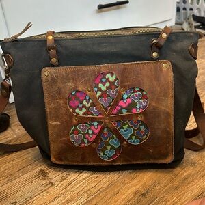 In blue black waxed canvas tote with leather pocket and flower handles